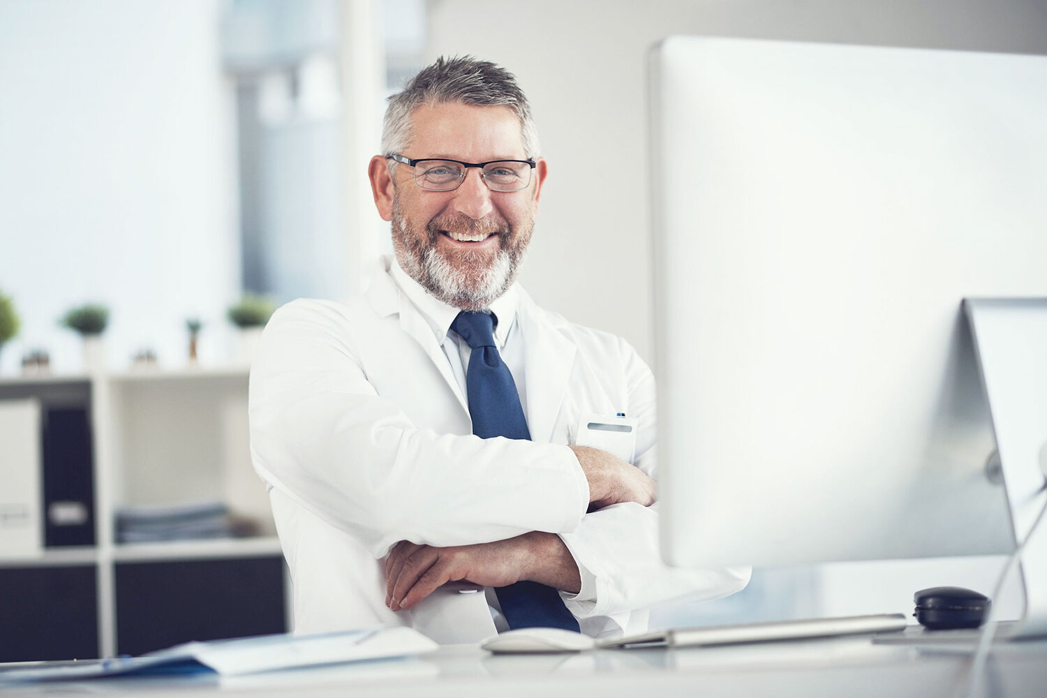 Experienced doctor sitting infront of his computer and smiles in the camera