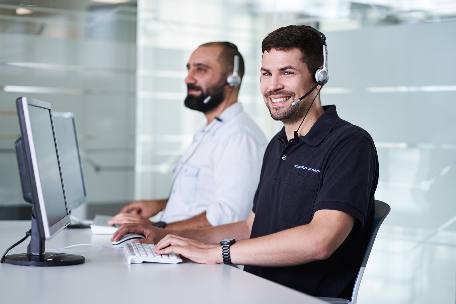 Zwei Männer mit Headsets sitzen vor Computerbildschirmen