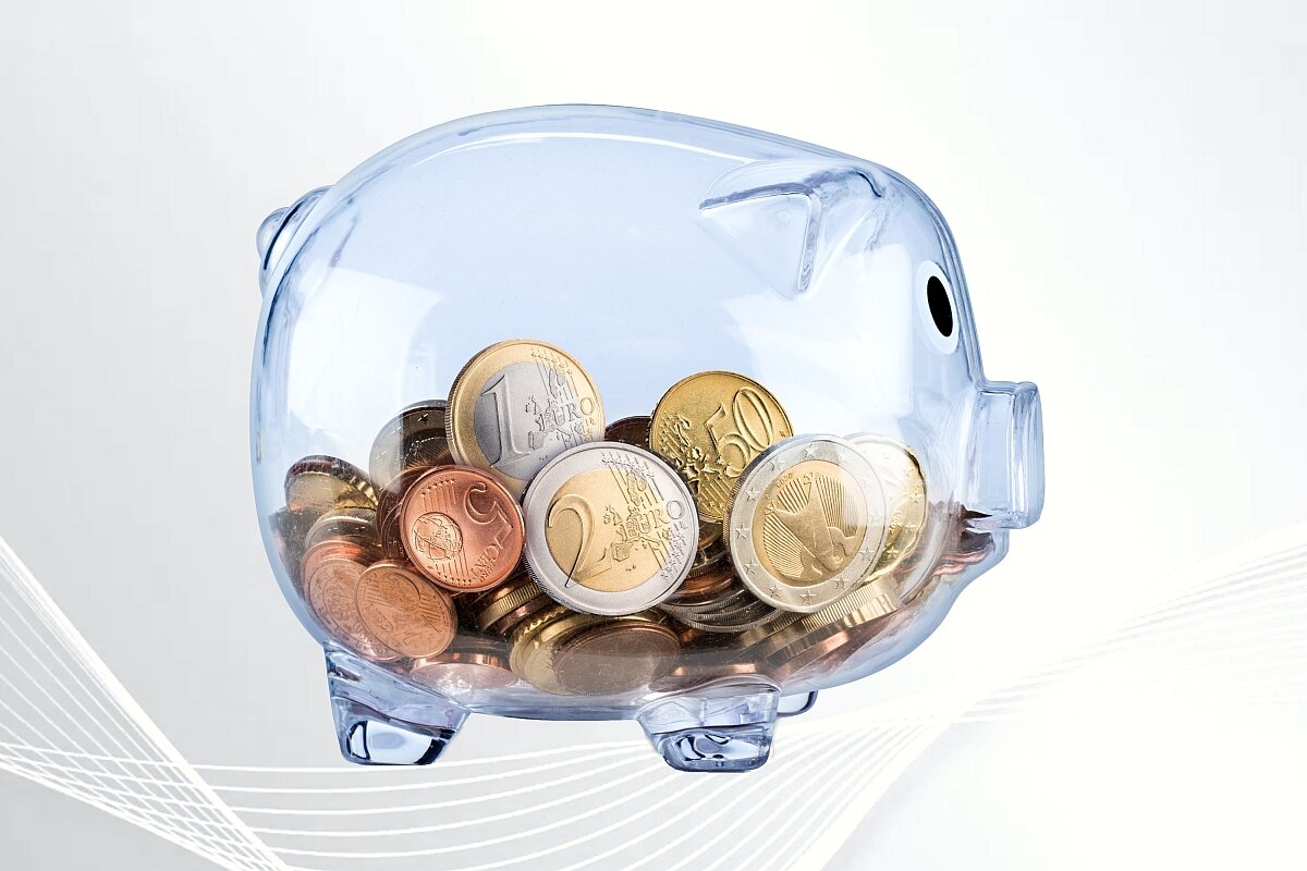 Transparent piggy bank with coins on light gray background